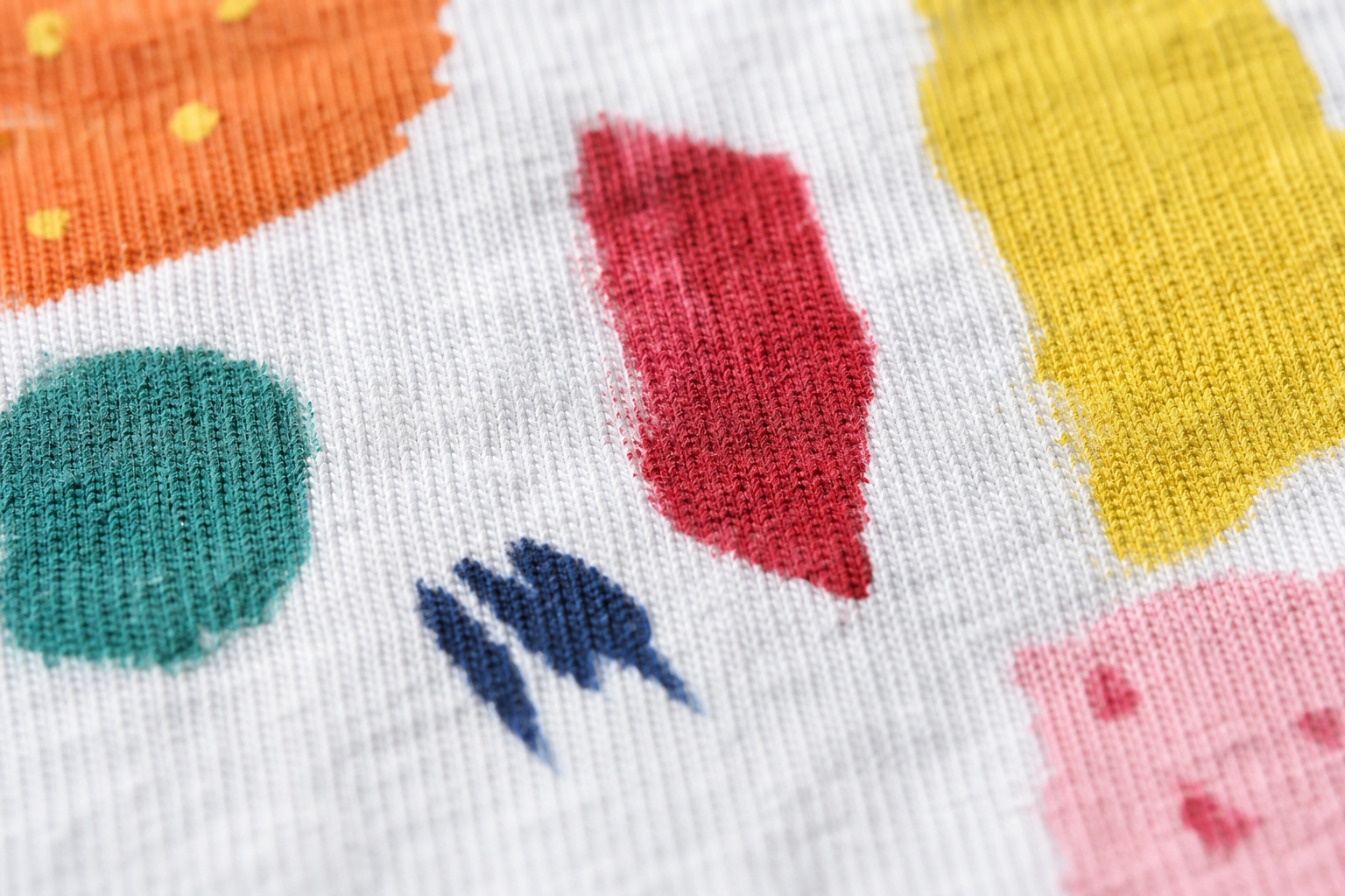 綿素材の白いTシャツにアクリル絵の具で描かれたカラフルなイラストのアップ写真。生地の織り目に絵の具が染み込んでいる質感が分かるクローズアップ、自然光、マクロ撮影風